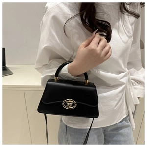 Close-up of a black trapezoid crossbody bag featuring a gold oval clasp and top handle