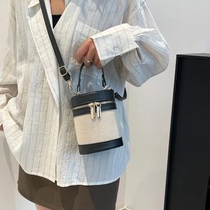 Fashionable cylinder bucket bag in beige canvas and black leather with gold zipper detail
