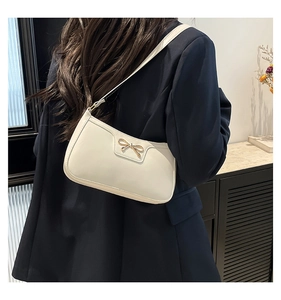 Détail d'un sac sous le bras crème avec boucle nœud doré porté sur un costume bleu