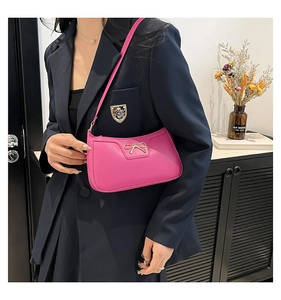 Detail of hot pink underarm bag featuring a golden metal bow and smooth leather texture
