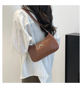 Detail of brown leather underarm bag featuring a golden metal bow and adjustable strap