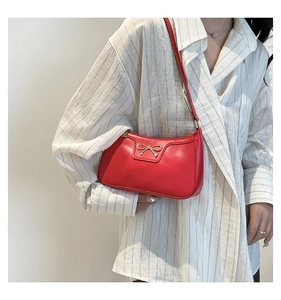 Détail d'un sac sous le bras en cuir rouge avec nœud métallique sur un mannequin en chemise