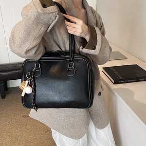 Minimalist black leather tote bag with white contrast stitching and baseball charm