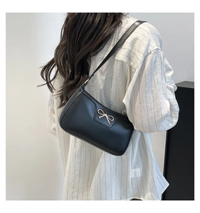 Détail d'un sac baguette noir chic avec un nœud doré et une fine bandoulière élégante