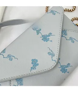 Close-up of light blue floral envelope bag with gold chain strap and grain texture