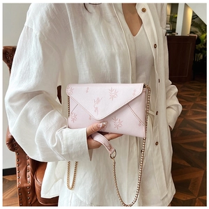 Pink floral envelope crossbody bag with a delicate gold chain strap on a white shirt