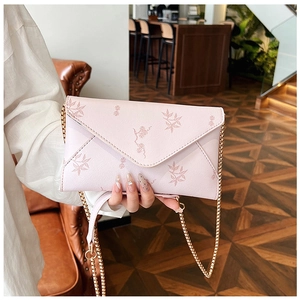 Detail of light pink envelope bag with floral leaf prints and a gold chain strap