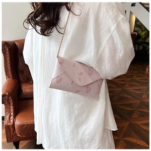 Close-up of a pink floral envelope bag with a delicate gold chain strap on a white shirt