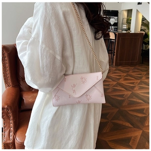 Detail of pink floral envelope bag with gold chain strap worn by model in a cafe