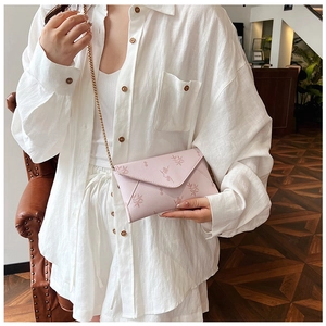 Detail of pink floral envelope bag with gold chain strap worn by model in hallway