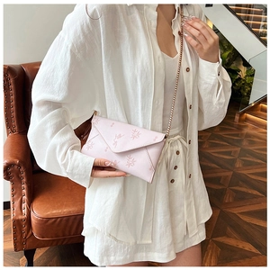 Detail of light pink envelope crossbody bag with leaf patterns and thin metal chain strap