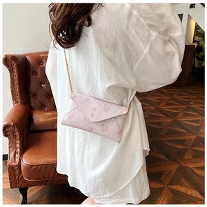 Close-up of pink floral envelope crossbody bag with gold chain strap on white shirt