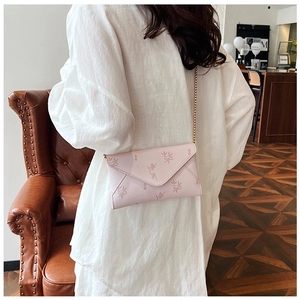 Pink envelope crossbody bag with floral texture and gold chain strap worn by a model