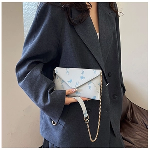 Detail view of light blue floral envelope bag with gold chain strap on grey blazer