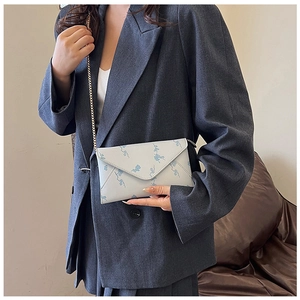 Detail of grey envelope chain bag with blue floral print and golden metal shoulder strap