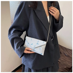 Detail of white envelope chain bag with blue floral print on an oversized grey blazer