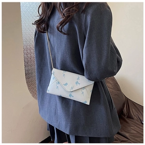 Detail of a beige envelope crossbody bag with angel print and a gold chain strap