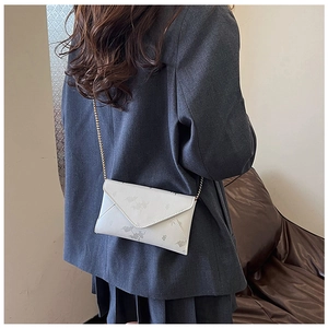 Chic cream envelope crossbody bag with floral pattern and gold chain on gray outfit