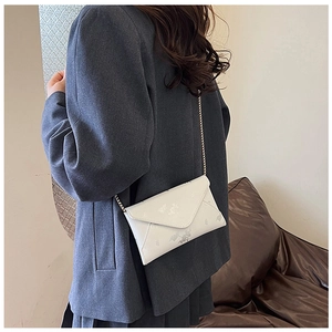 White envelope bag with chain strap styled on shoulder with a grey suit blazer