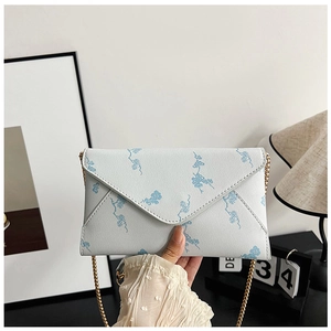 Close-up of white envelope chain bag featuring light blue floral patterns and gold chain