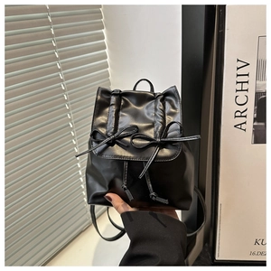 Détail d'un mini sac à dos noir avec nœuds en cuir et fermeture à cordon tenu en main