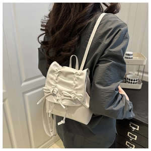 Detail of white mini leather backpack featuring decorative bows and pleated design