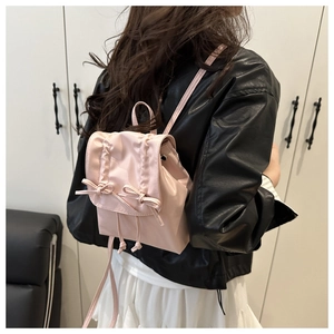 Vue arrière d'un mini sac à dos rose avec des nœuds sur un mannequin en veste noire
