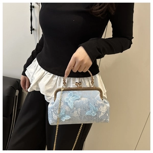 Detailed close-up of light blue floral embroidery with butterfly accents and gold chain handle
