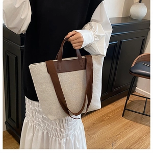 Side view of a beige canvas tote bag with brown leather handles and wide shoulder strap