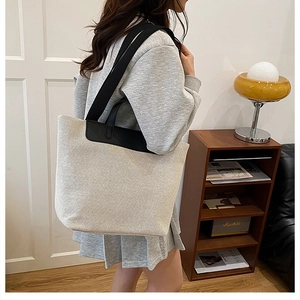 Detailed side view of a large canvas tote bag with black leather trim and dual straps