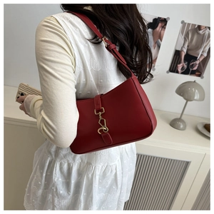 Detail of a dark red leather shoulder bag with a gold metal buckle on a female model