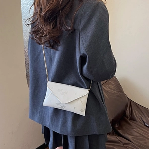 Chic white envelope crossbody bag with floral patterns and gold chain strap on model