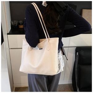 Détail du sac cabas crème avec texture grainée et plaque logo en métal bleu sur le devant