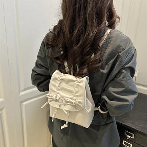 Mini sac à dos blanc plissé en cuir avec nœuds porté par un mannequin dans un décor épuré
