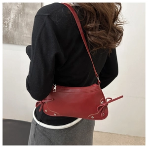 Dettaglio borsa rossa a mezzaluna con fiocchi laterali decorativi e rivetti metallici alla base