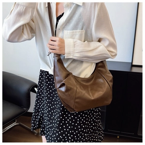 Dark brown pleated leather hobo bag worn by a model in a modern indoor lifestyle setting