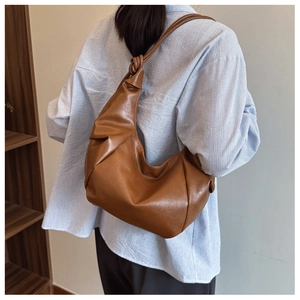 Close-up of brown PU leather dumpling bag with soft pleated texture and knotted shoulder strap
