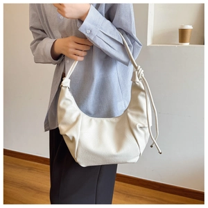 Chic cream dumpling bag with knot detail and tassels worn in an urban setting