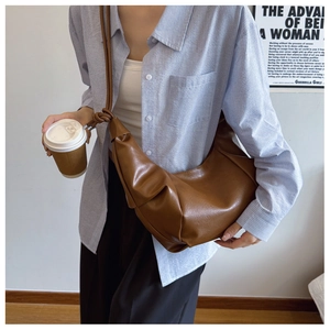 Brown faux leather dumpling bag with knotted strap detail shown on model in modern room