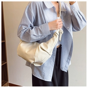 Detail of cream white leather dumpling bag with knotted strap on blue striped shirt