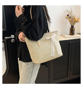 Close-up of beige woven tote bag with white lace bow and leather handle details