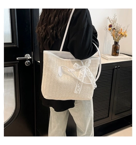 Close-up of cream woven tote bag featuring white lace bow and fine V-shaped straw texture