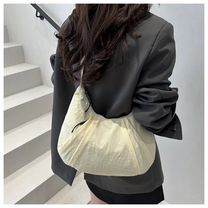 Détail du sac demi-lune en nylon crème avec texture plissée sur un blazer gris