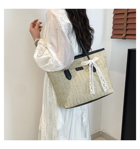 Détail d'un grand sac cabas en paille avec poignées noires et un nœud en dentelle blanche