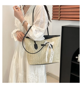 Detail of summer straw tote bag featuring elegant white lace bow and black PU leather strap