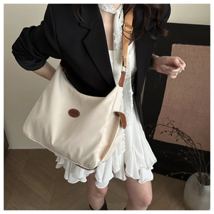 Detail of a large beige nylon crossbody bag featuring an oval leather fashion patch