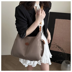 Detail of a brown nylon tote bag with a leather Fashion patch shown on a stylish model