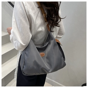 Detail view of large gray nylon shoulder bag with adjustable brown strap and logo patch