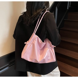 Borsa tote in vernice rosa con nodi indossata a spalla in un ambiente dal design minimal
