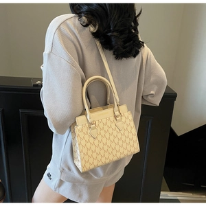 Close-up of stylish cream crossbody bag featuring vintage M-pattern and top handle detail